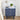 Navy blue nightstand with floral patterns, lamp, and books on a light wooden floor.