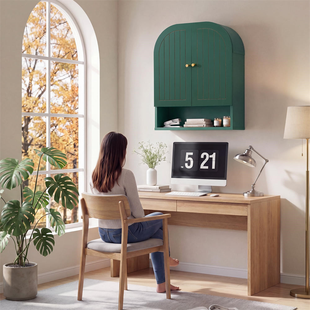 Person sitting at a wooden desk with a green wall-mounted cabinet, computer monitor displaying '5 21', and potted plant.
