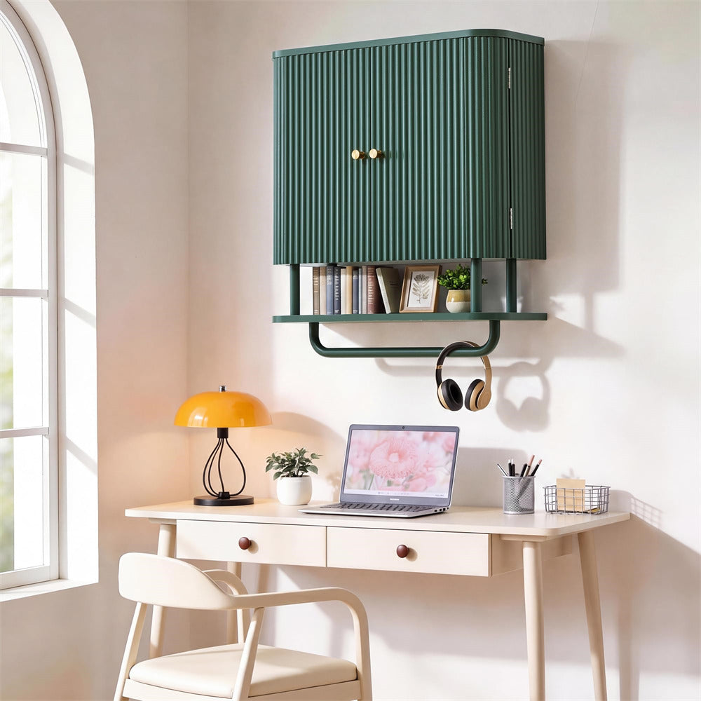 A dark green wall-mounted storage cabinet with vertical slats and gold knobs, styled above a light wood desk in a bright home office setting.