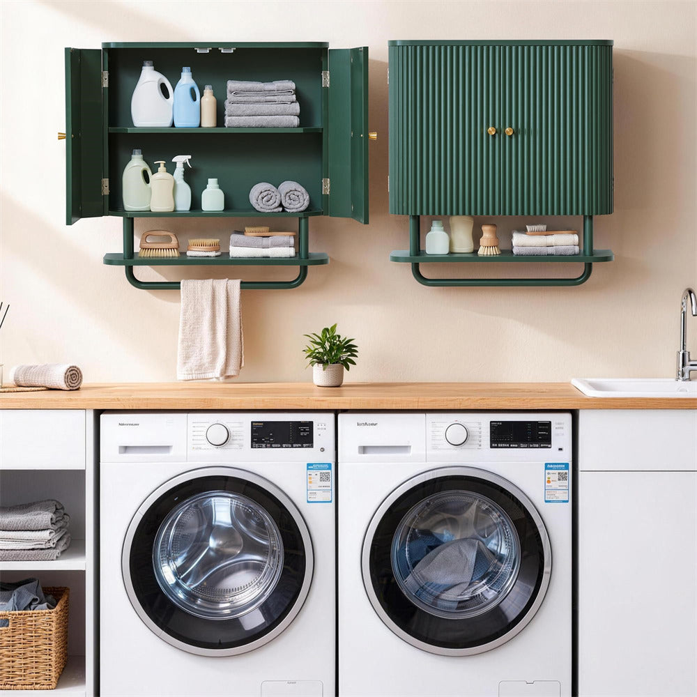 A modern laundry room setup featuring a pair of white front-loading washing machines beneath a wooden counter. Above the counter, two dark green wall-mounted storage cabinets are styled with towels, laundry detergent bottles, and small accessories.
