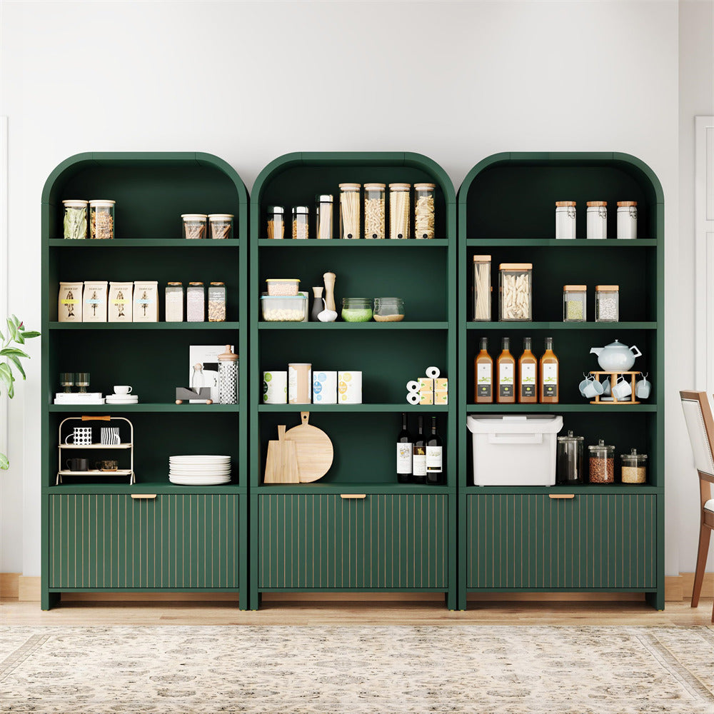 A three-compartment dark green kitchen pantry shelving unit with arched top frames, ribbed lower cabinet doors, and gold-tone handles, styled with kitchenware and jars against a white wall.