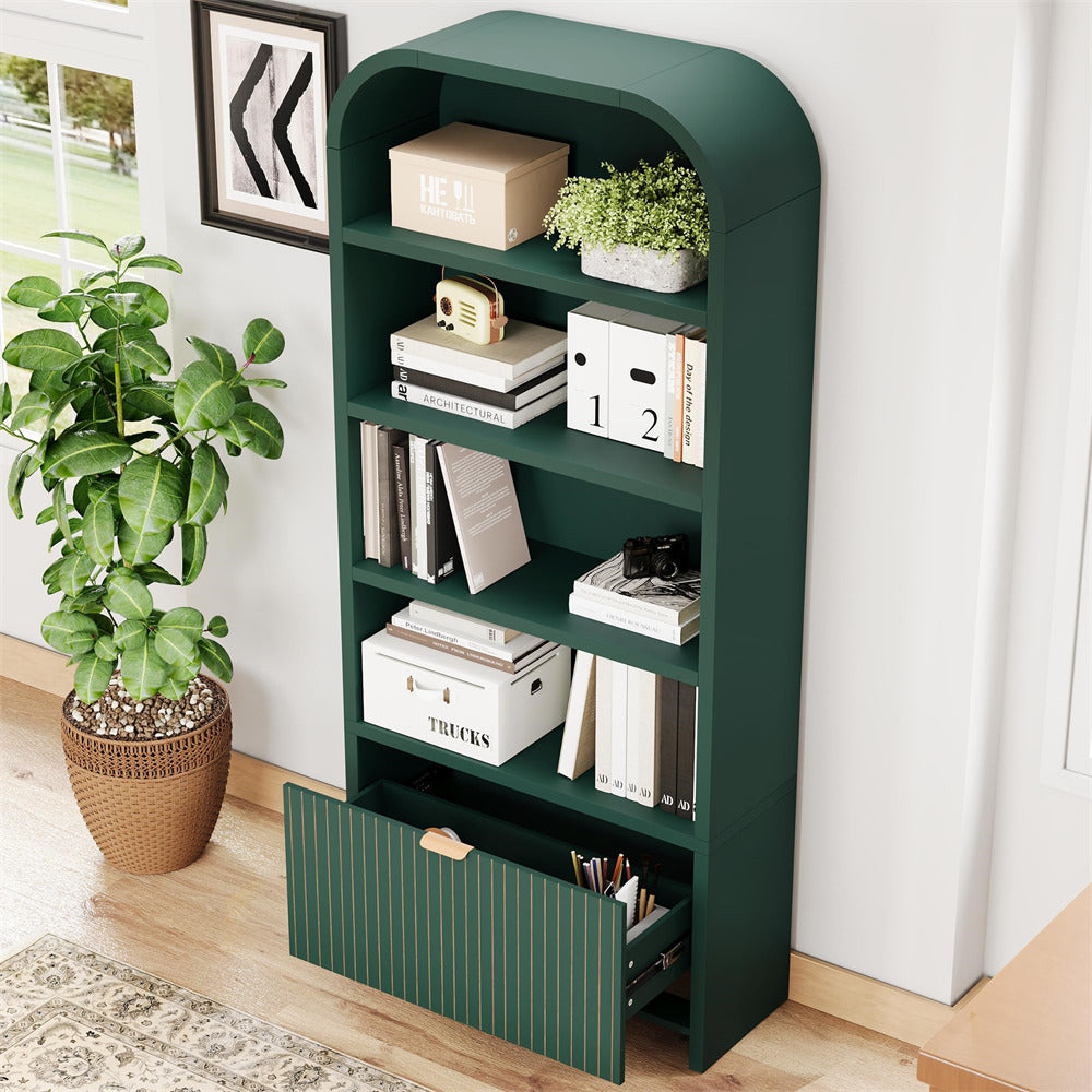 A dark green modular bookshelf with a rounded top, five open shelves, and a lower drawer, styled with books, boxes, and a small plant in a bright room.