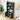 Green bookshelf with decorative items in a room with a plant and wall art.