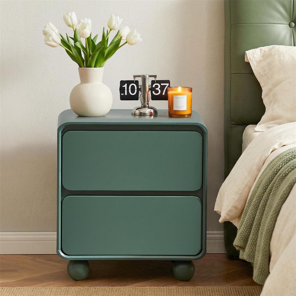 Green nightstand with a vase of white tulips, candle, and clock next to a bed.