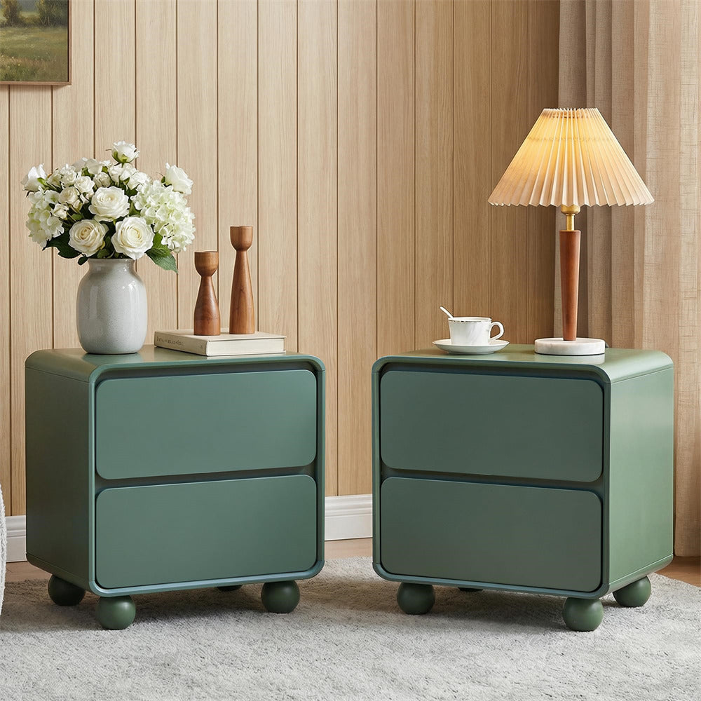 Two green nightstands with a lamp, flowers, and books against a wooden wall.