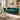 A classic Chesterfield-style sofa in deep emerald green velvet, styled in a luxurious, warm-toned living room with a marble coffee table, beige rug, and decorative plants.
