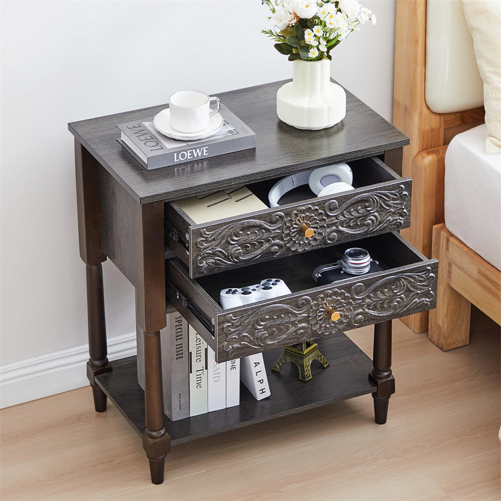 Decorative grey side table with embossed design, books, and a vase on a wooden floor.