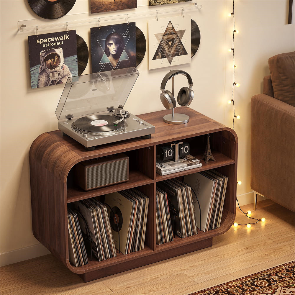 A dark brown wooden media console with rounded corners, styled in a cozy living room setting. The console features open shelves filled with vinyl records, a small clock, and a speaker, and a silver turntable with a clear lid sits on top.