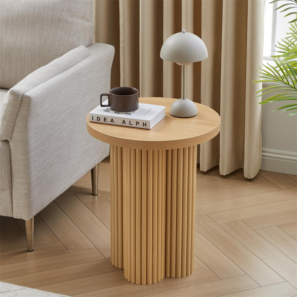 Round wooden side table with a lamp and books in a living room setting.