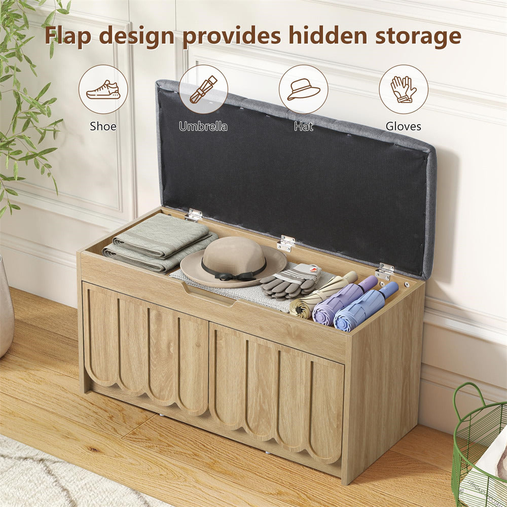 Wooden storage bench with a flap lid containing shoes, an umbrella, a hat, and gloves on a wooden floor.