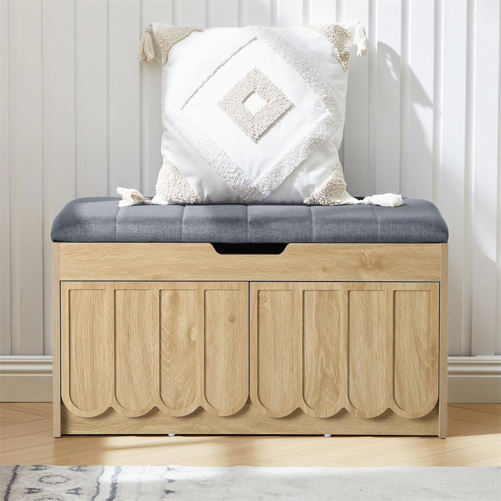 Wooden storage bench with a cushion and decorative pillow against a white paneled wall.