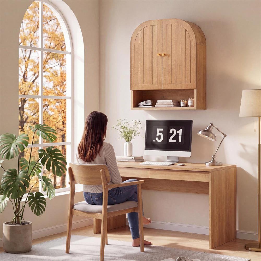 Person sitting at a wooden desk with a computer, surrounded by plants and a large window with autumn foliage.