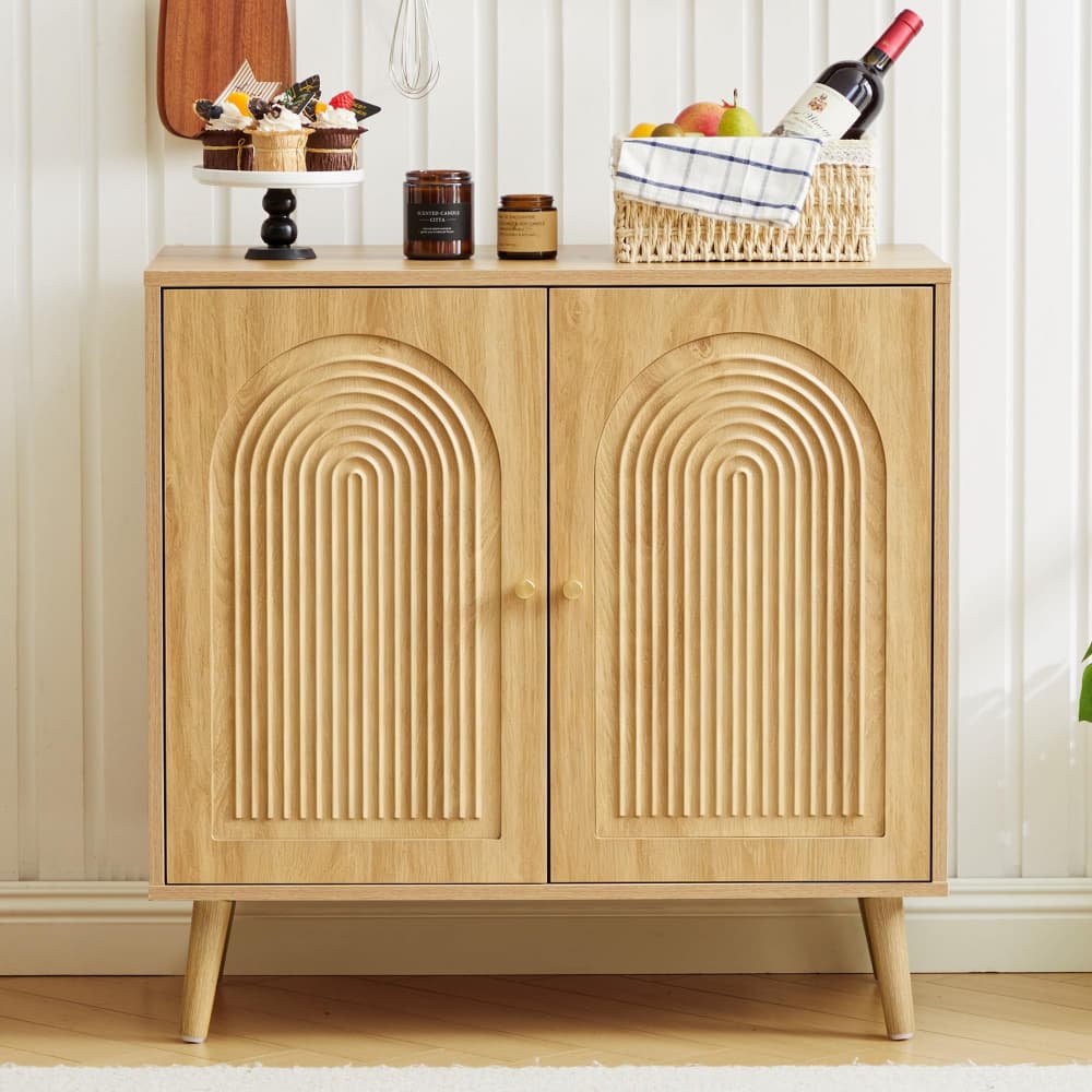 A light natural wood sideboard cabinet with two doors featuring a raised arched rib pattern, styled with food and drink items on top against a white paneled wall.