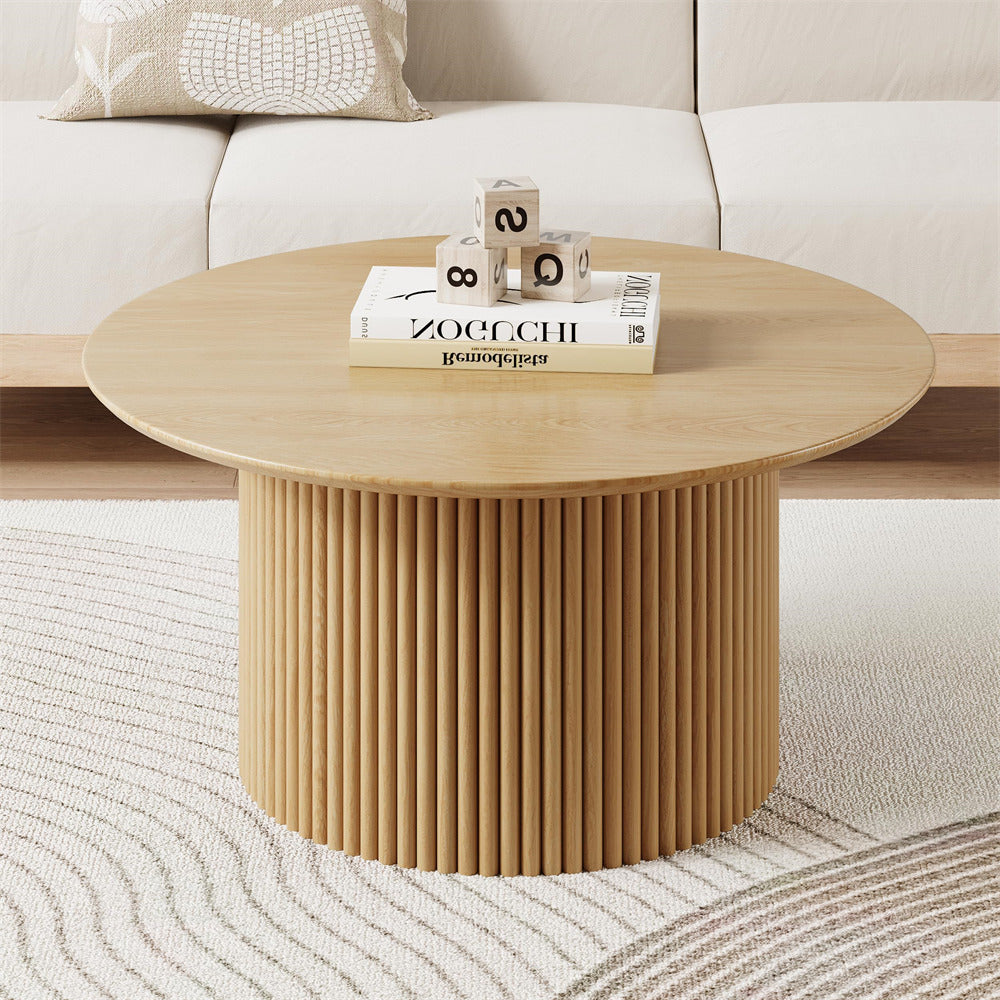 Round wooden coffee table with books and decorative items in a living room setting.