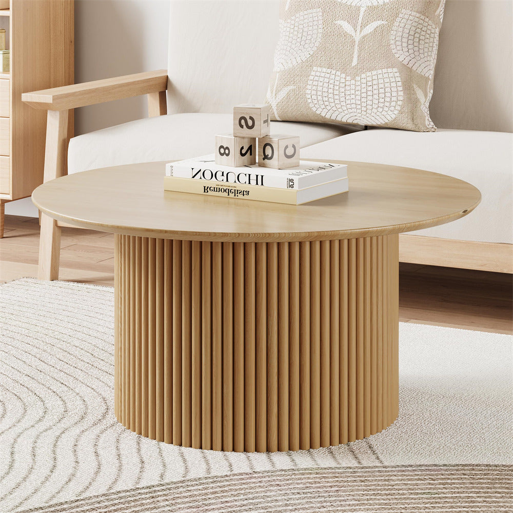 Round wooden coffee table with a ribbed cylindrical base in a living room setting.
