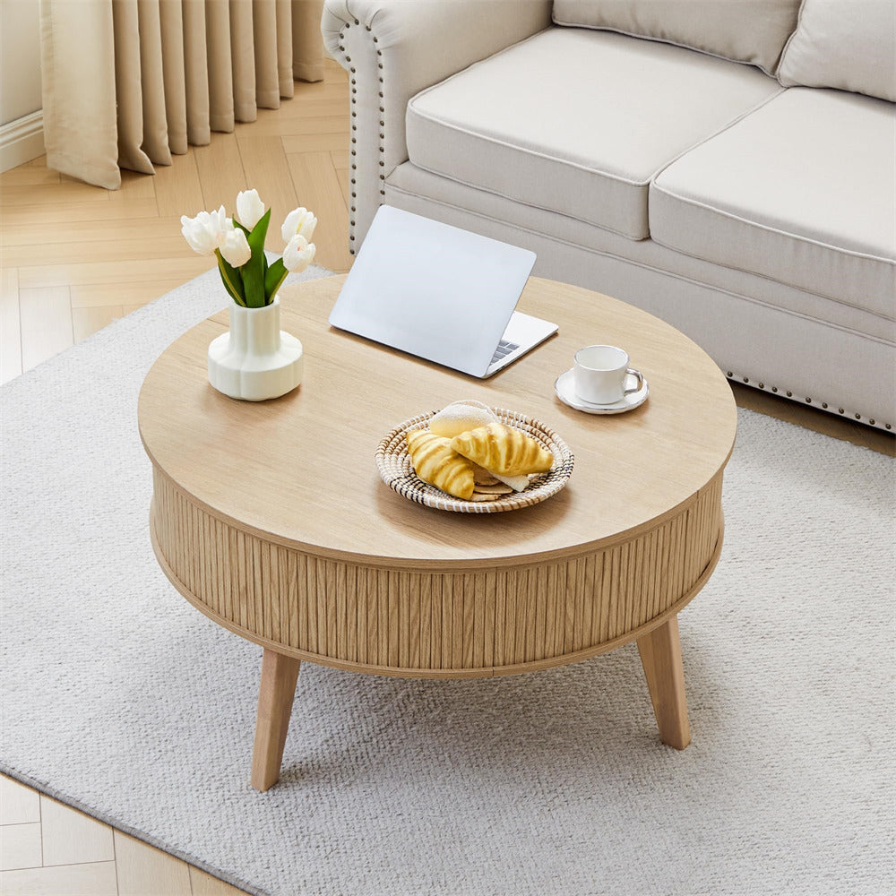 Round wooden coffee table in a living room with a laptop, cup, and plate of food.