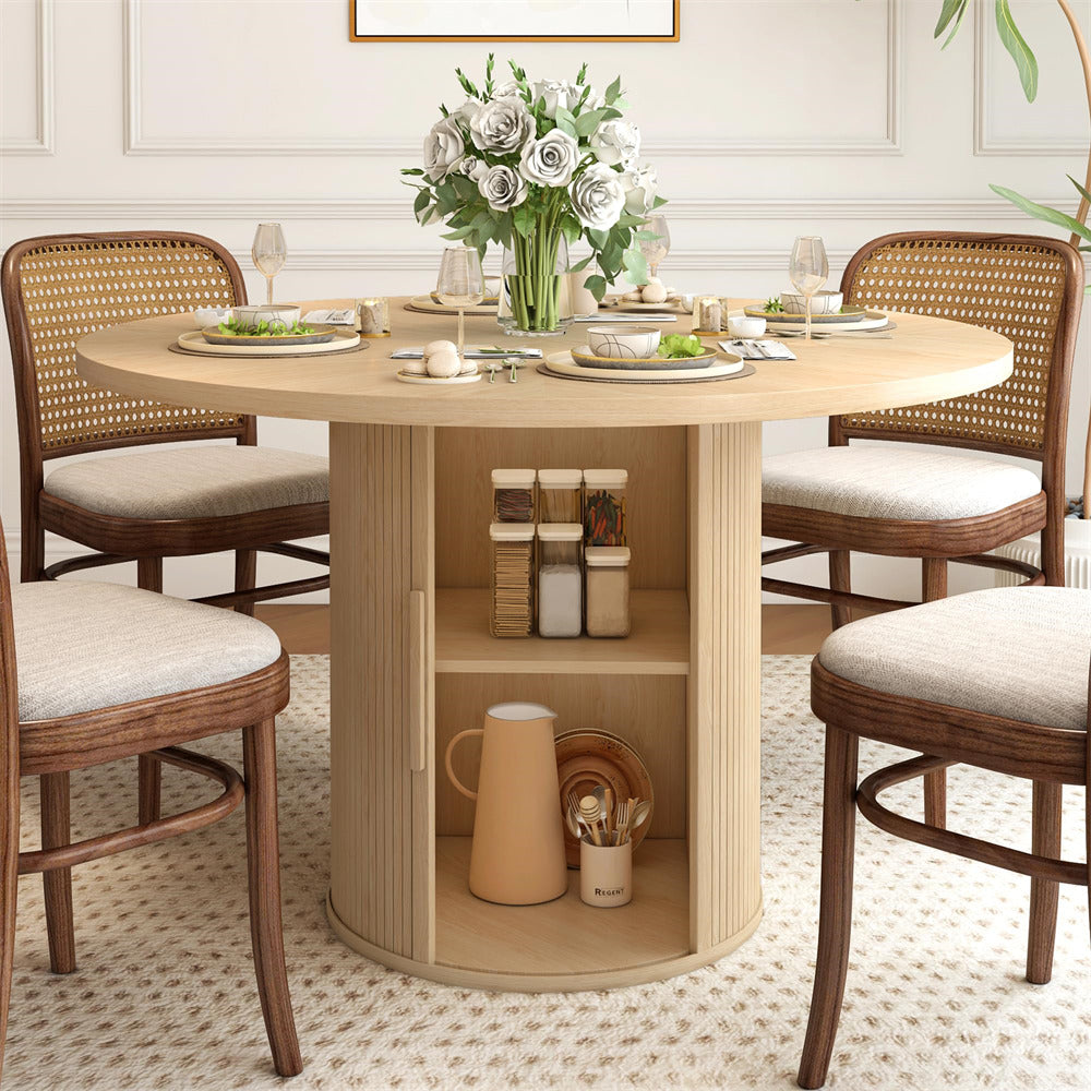 Round wooden dining table with chairs in a well-lit room, featuring a vase of flowers on the table.