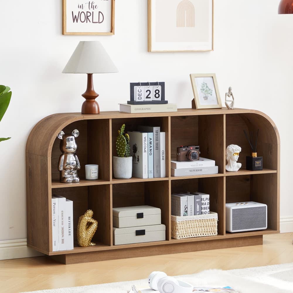A wooden arched bookcase with open cubbies, styled in a bright room with books, a lamp, decorative figurines, and storage boxes.