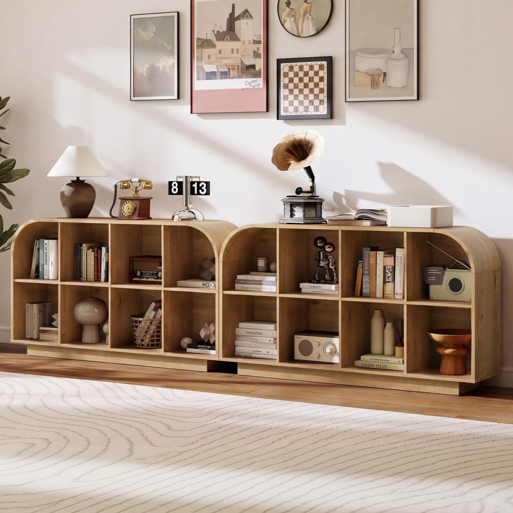 A light natural wood modular bookcase with arched compartments, styled in a cozy living room setting with books, a lamp, a gramophone, and framed wall art.