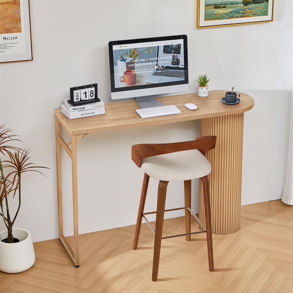 Wooden desk with computer setup and bar stool in a room with decor elements.