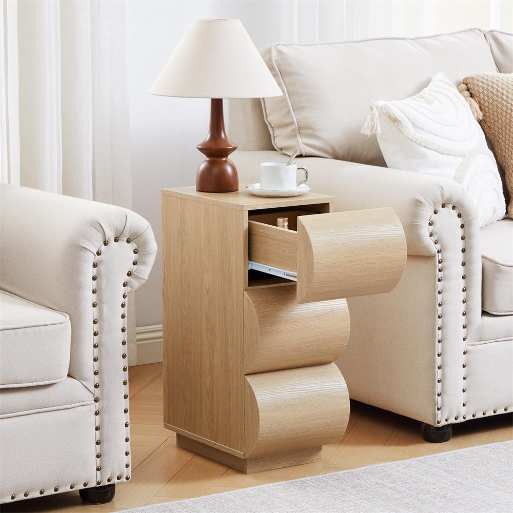 Wooden side table with a lamp and cup next to a beige sofa and armchair in a living room.