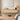A modern floating wooden console shelf mounted on a beige wall in a styled bedroom or living space, holding decorative objects and a lit table lamp. A bed with a green knit throw is partially visible in the foreground, along with a woven rug and a robotic vacuum on the floor.