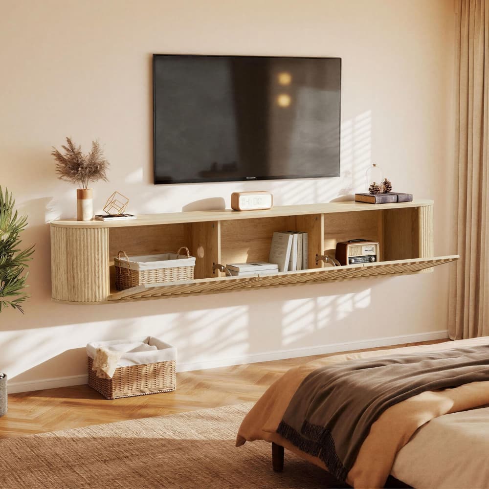 A floating wall-mounted TV stand and shelf unit in a warm light wood finish, styled in a modern bedroom setting with a wall-mounted TV, baskets, books, and a bed visible in the room.
