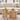 Two round nesting coffee tables with fluted pedestal bases in a warm light wood finish, styled in a bright living room with a beige sofa and decorative items on top.