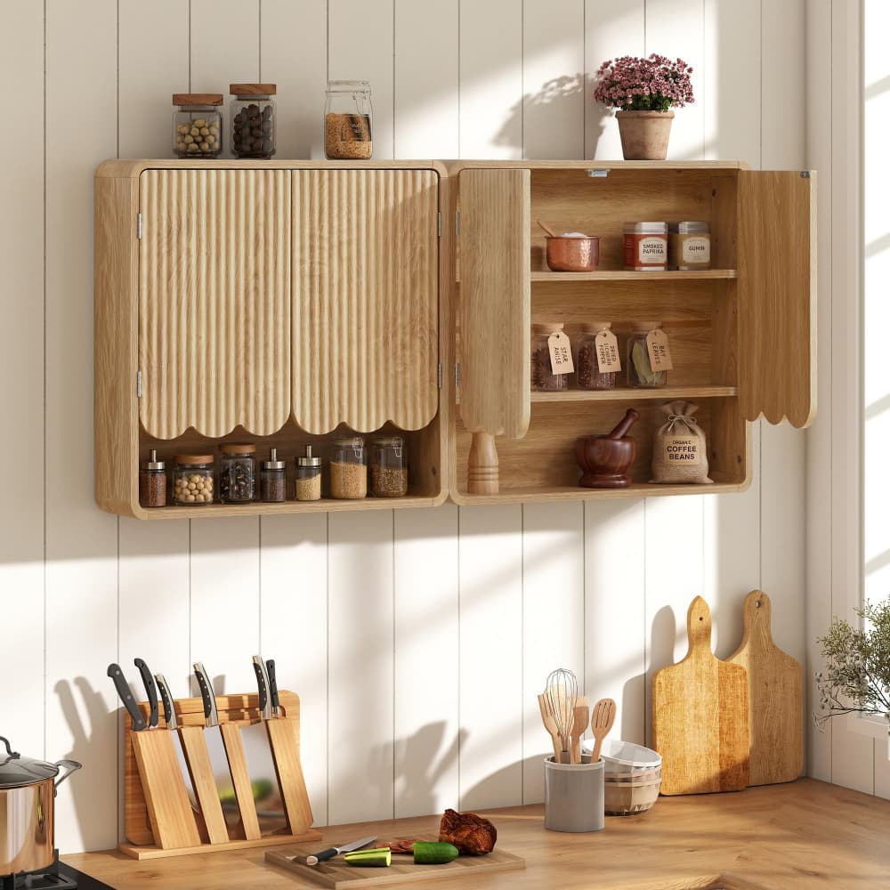 A light natural wood wall-mounted kitchen cabinet with scalloped doors, shown open with shelves and spice jars inside, set against a white paneled wall in a styled kitchen scene.