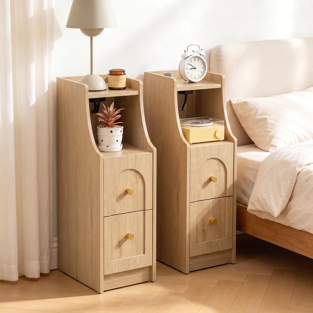 Two light wood bedside tables with two drawers and open shelving, styled in a bedroom next to a bed with beige bedding.