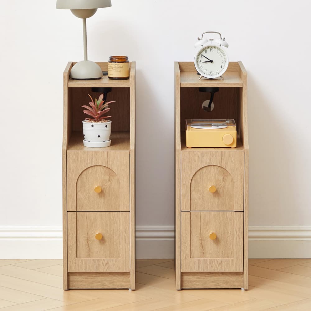 Two light oak wood nightstands with two drawers and open shelving, styled with home decor items against a white wall and light wood floor.
