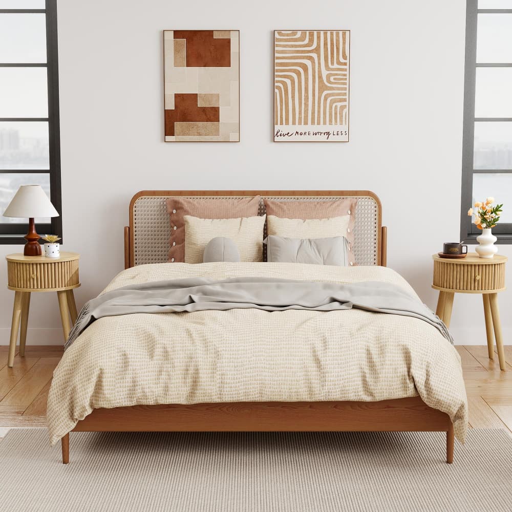 A wooden bed frame with a woven cane headboard, styled with beige and gray bedding, flanked by two matching wooden nightstands in a bright, modern bedroom.