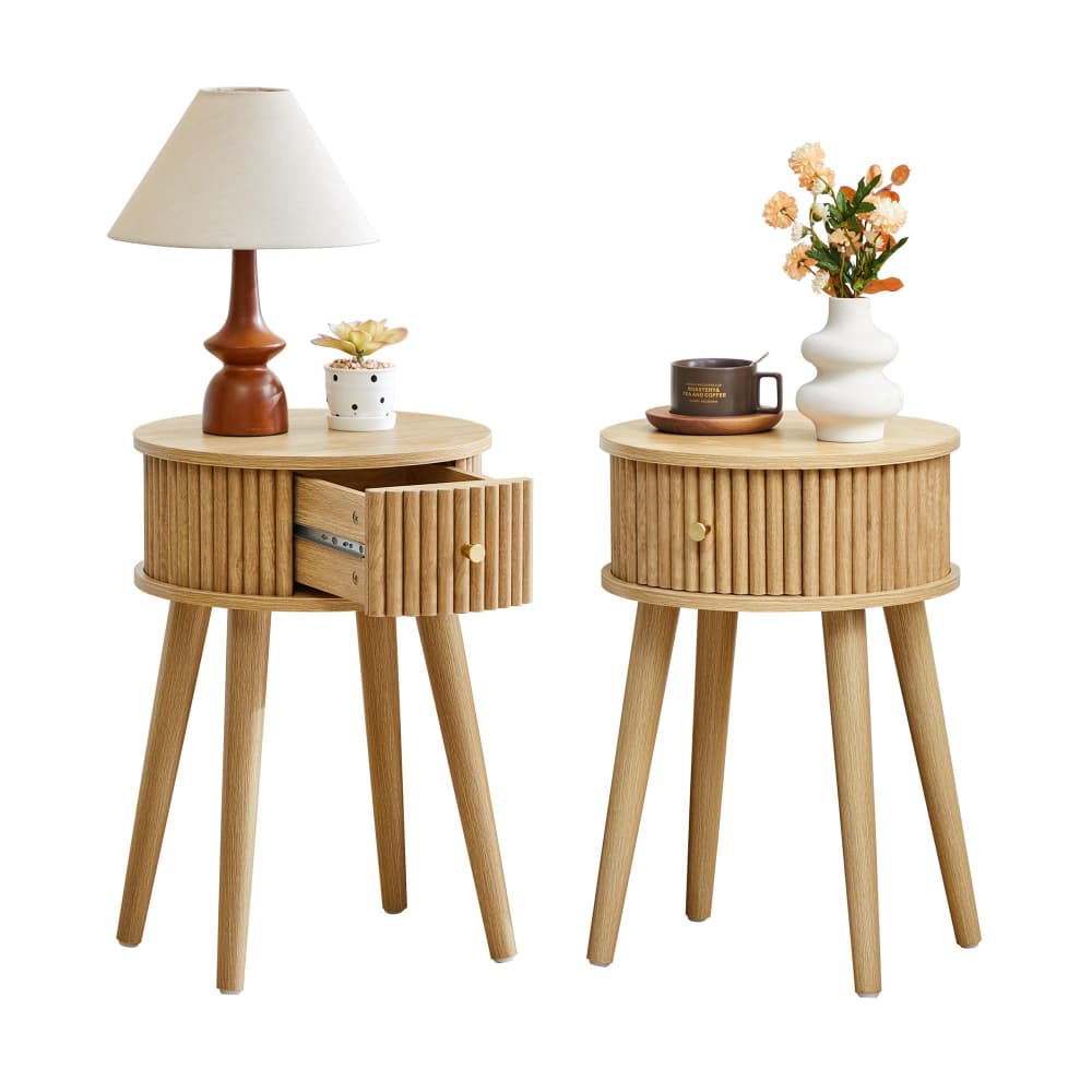 Two light natural wood side tables with slatted cylindrical bodies and tapered legs, shown on a white background. The left table has a drawer and is styled with a table lamp and small vase; the right table has a single drawer and is styled with a mug and vase of flowers.