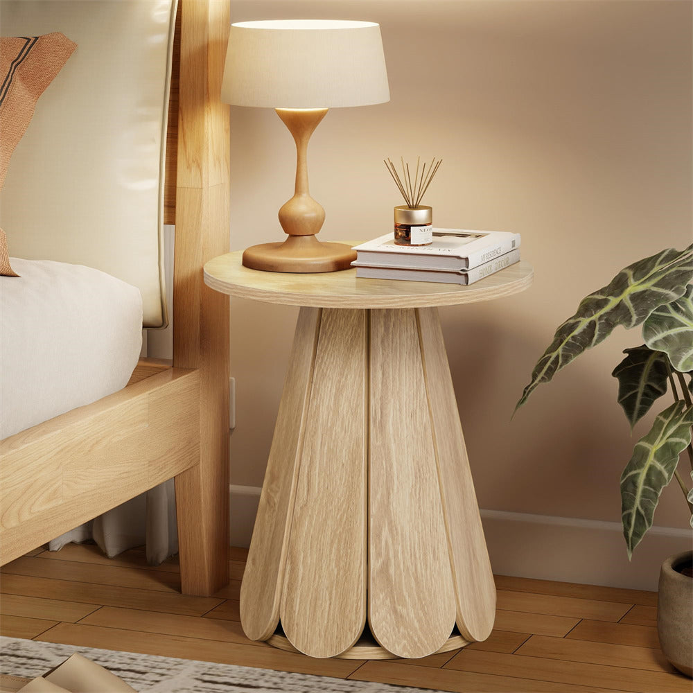 Wooden side table with lamp and decor items next to a bed in a bedroom.