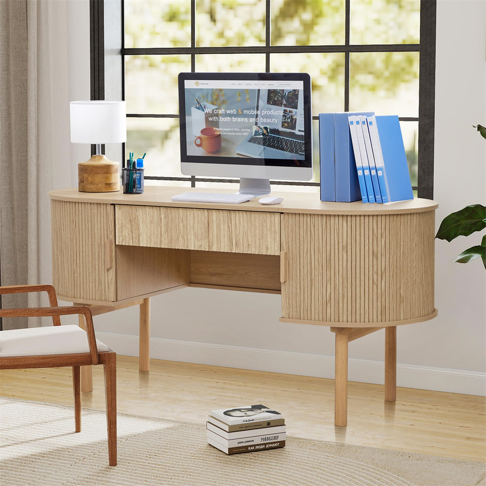 Wooden desk with computer setup in a bright room with large windows.
