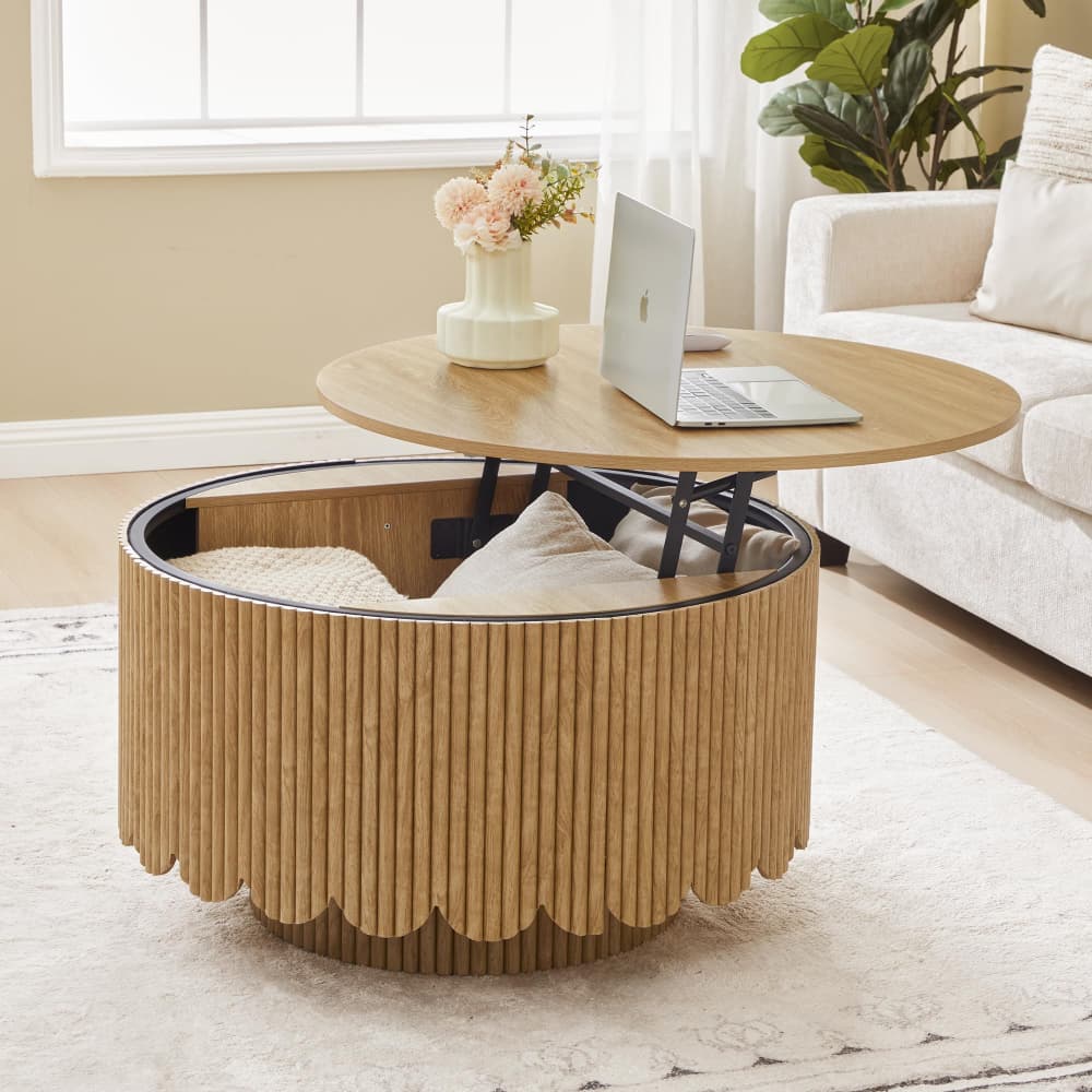 A round wooden coffee table with a fluted slatted base and a separate round wooden top, styled in a bright living room with a laptop and vase of flowers on the tabletop.