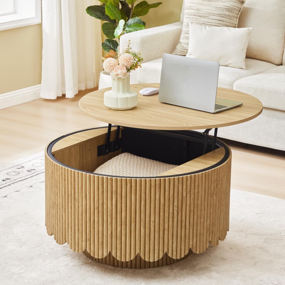 A round lift-top coffee table in a warm light wood finish, styled in a bright living room. The table features a fluted slatted lower body with a scalloped edge, a black metal trim, and a lift-up top surface holding a laptop and flowers.