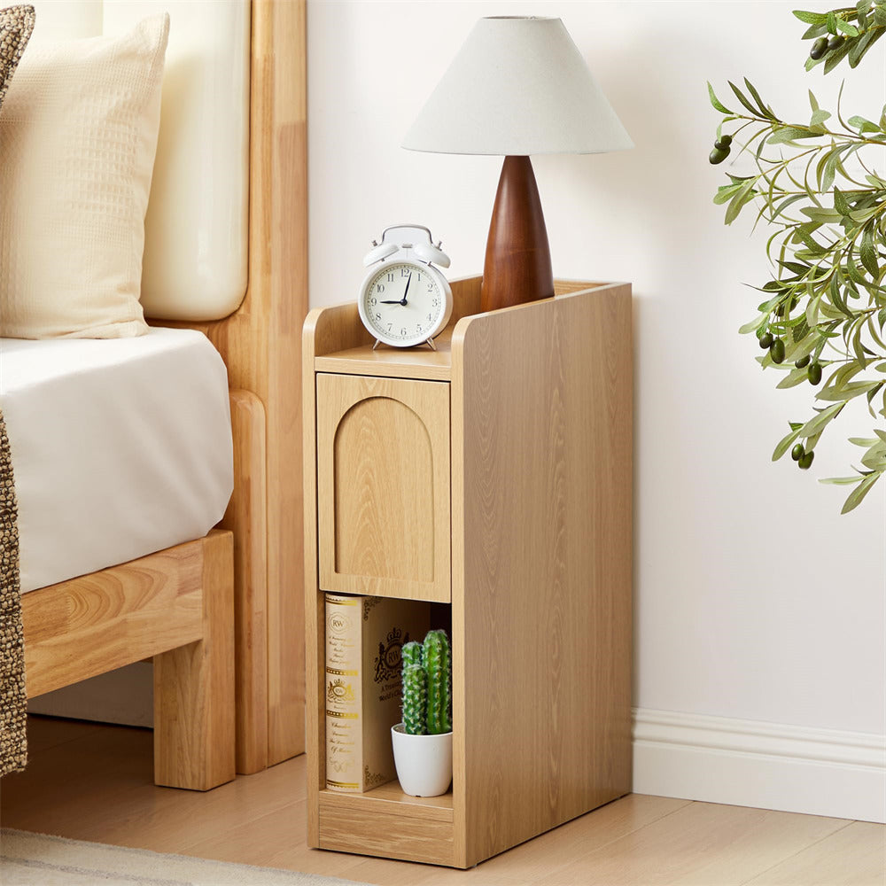 Wooden nightstand with lamp, clock, and books next to a bed in a bedroom.
