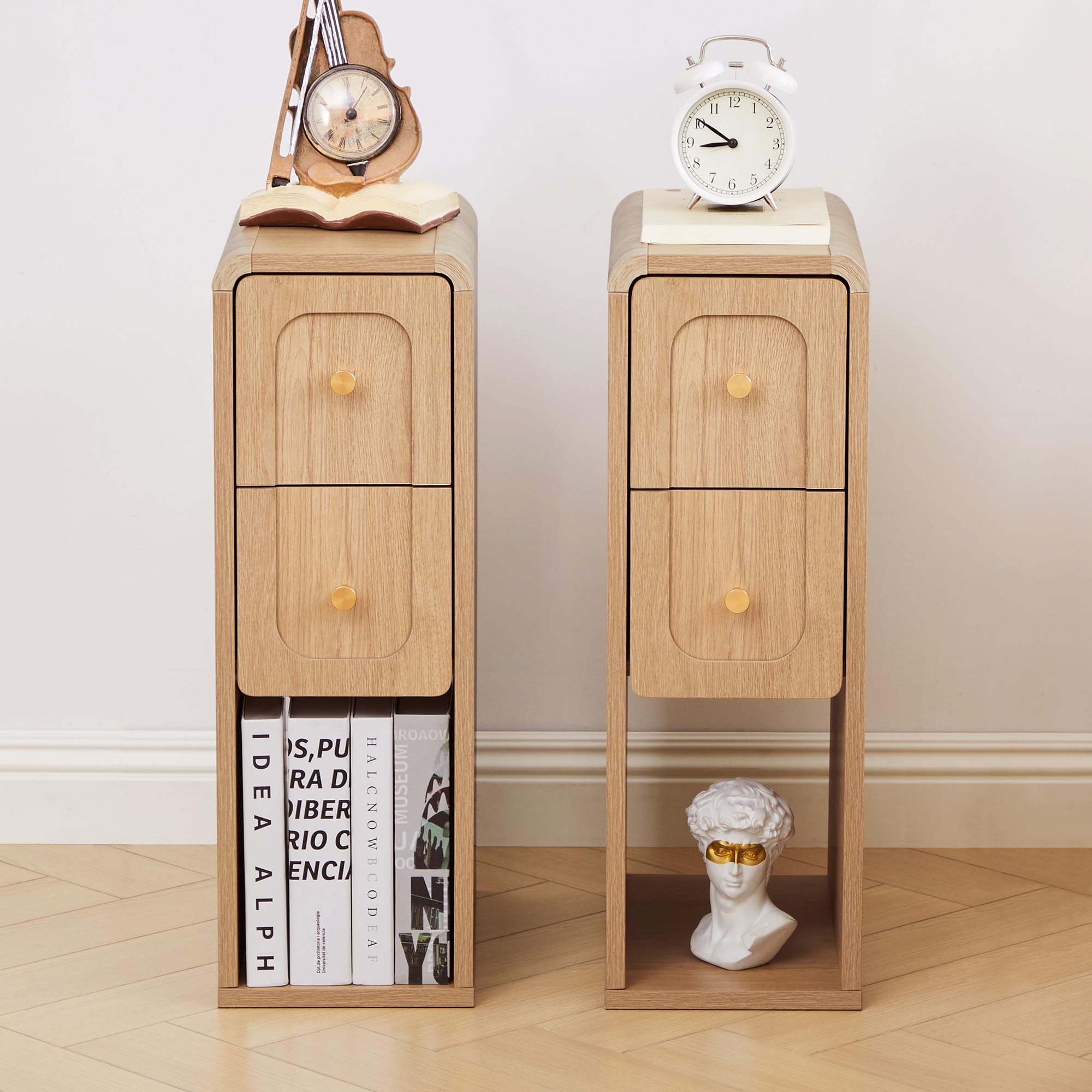 Two matching light wood nightstands with two drawers and open lower shelves, styled in a room setting with books, a clock, an alarm clock, and a small bust on top and in the shelf.