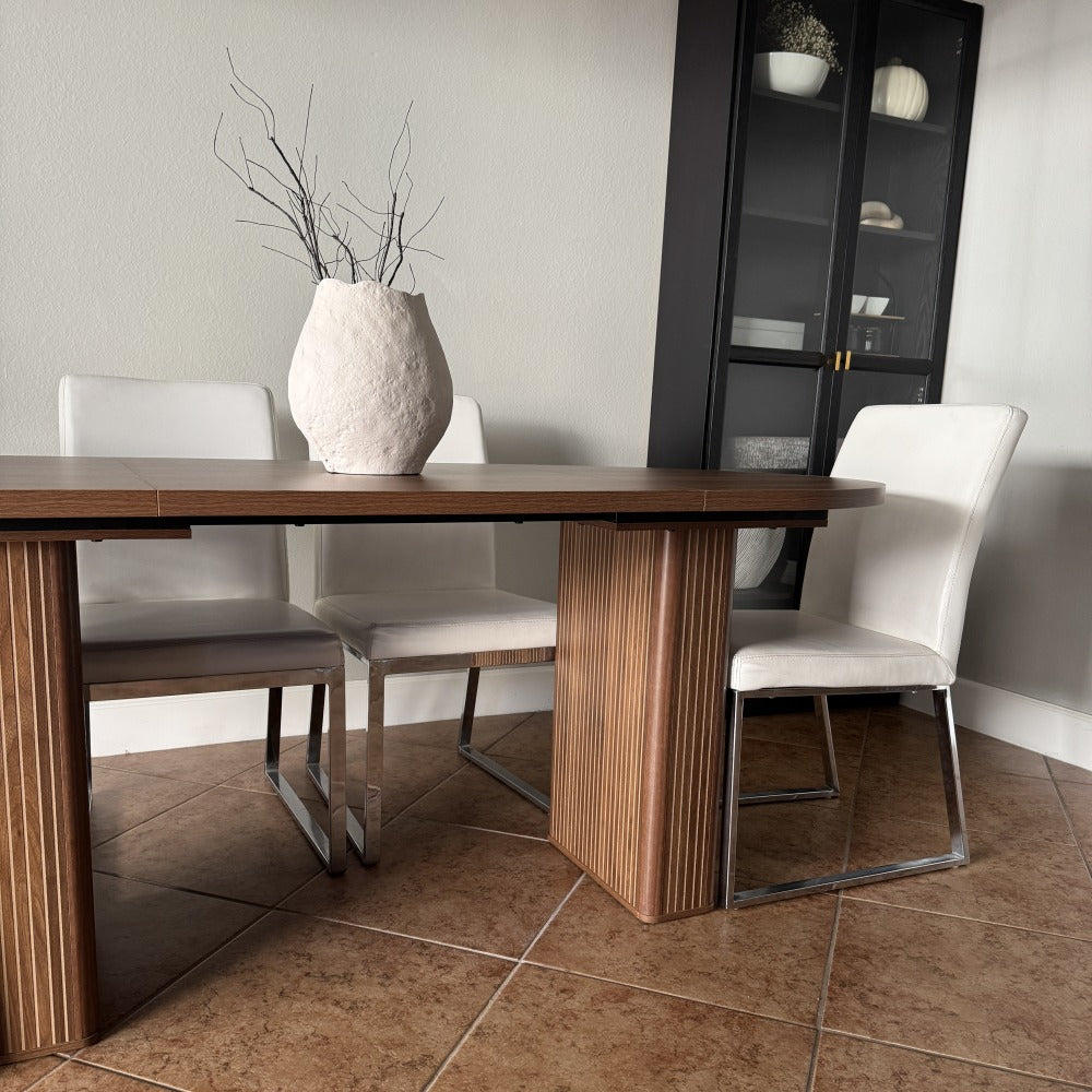 Dining room with wooden table, white chairs, and a vase on the table.