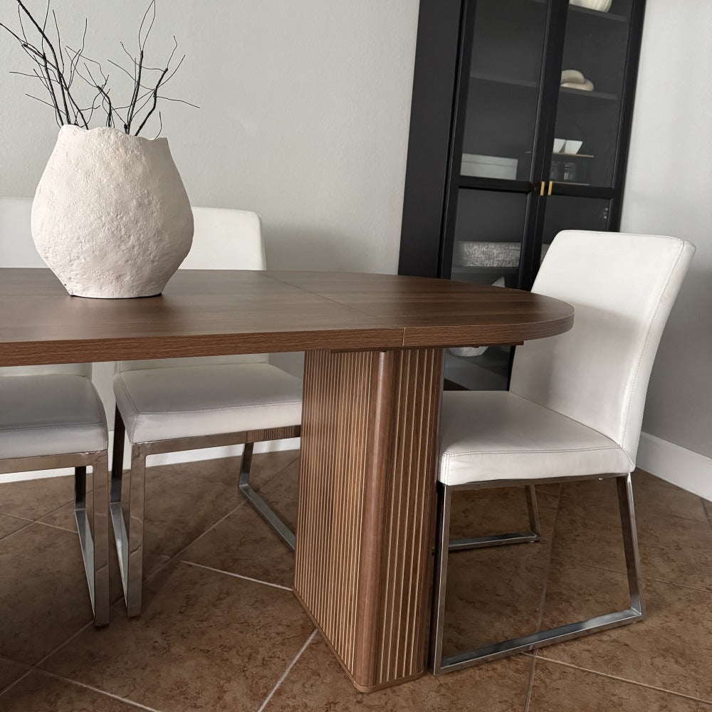 Dining table with four chairs and a vase in a room with a gray wall and tiled floor.