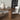 Dining table with four chairs and a vase in a room with a gray wall and tiled floor.