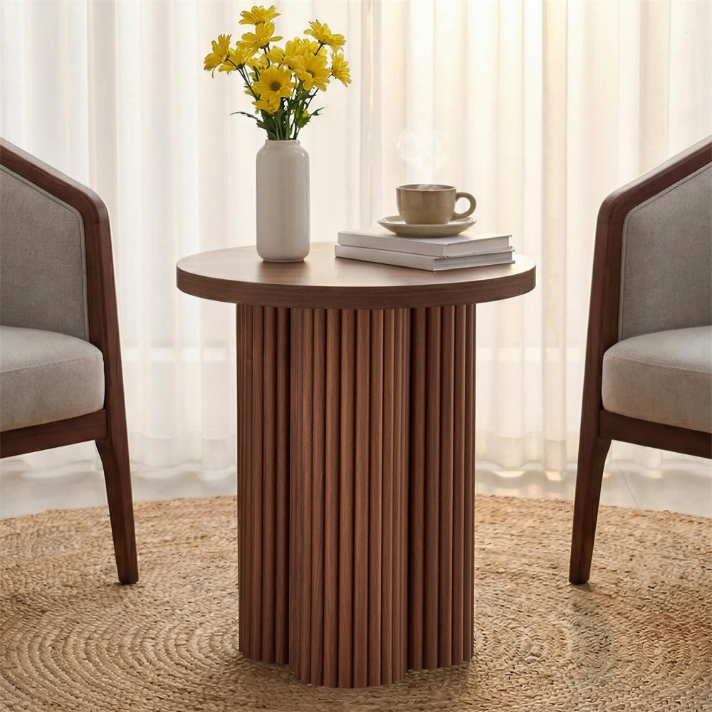 Round wooden side table with a vase of yellow flowers and a cup in a living room setting.