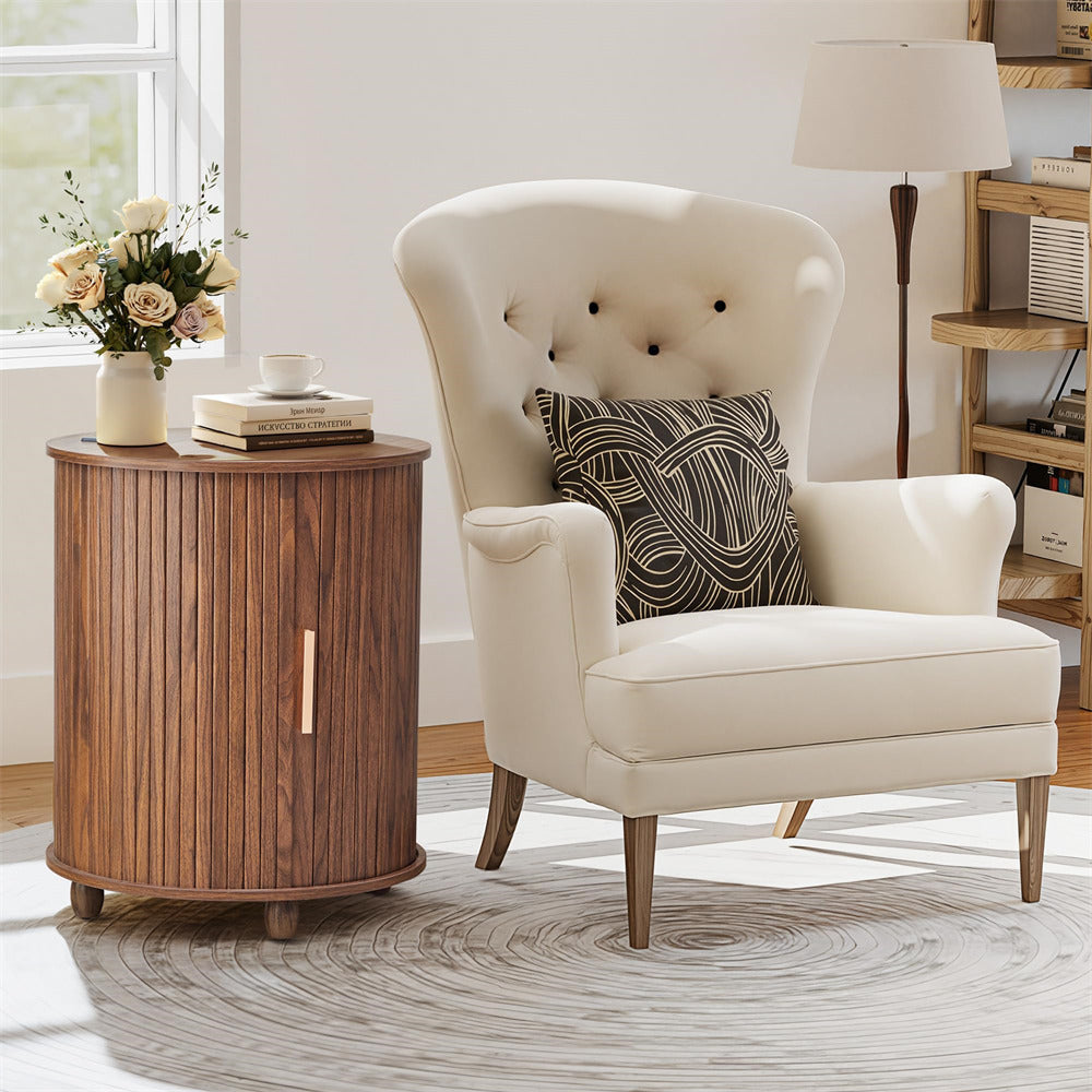 White armchair with a patterned pillow next to a wooden side table in a room with a lamp and window.