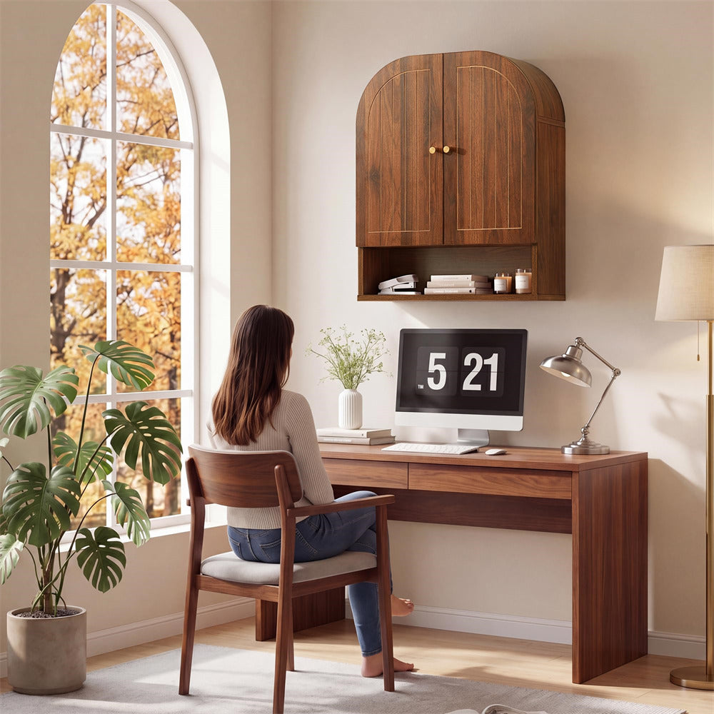 Person sitting at a wooden desk with a computer, surrounded by plants and a large window with autumn foliage.
