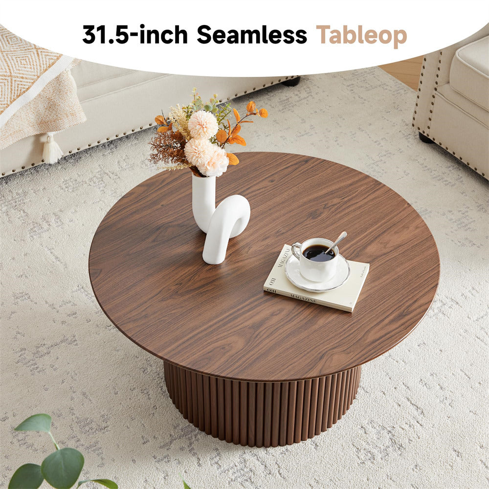 Round wooden coffee table with a vase of flowers and a cup on top, in a living room setting.