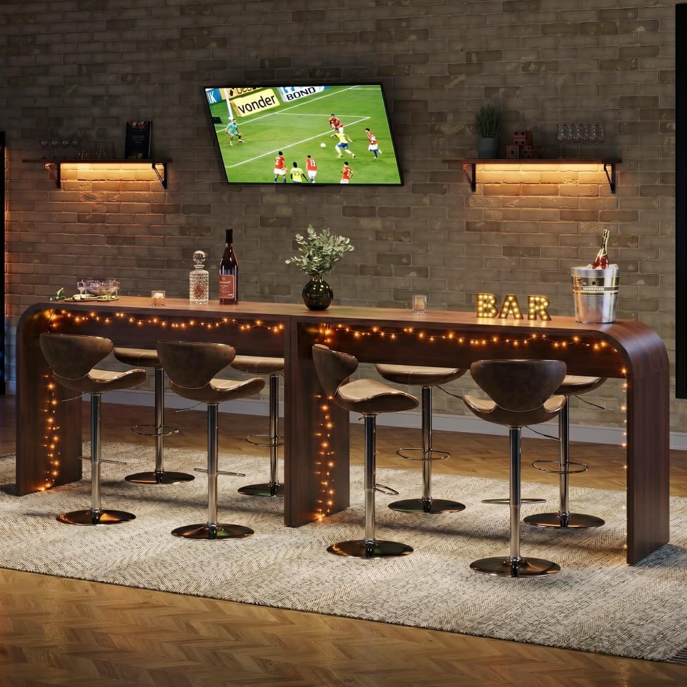 A modern curved wooden high bar with six bar stools, decorated with warm string lights, set in a cozy room with a brick wall and a mounted TV.