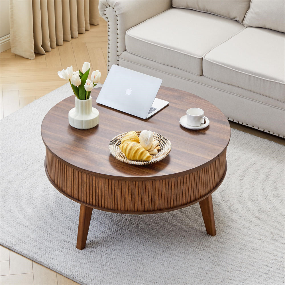 Round wooden coffee table in a living room with a laptop, cup, and snacks.