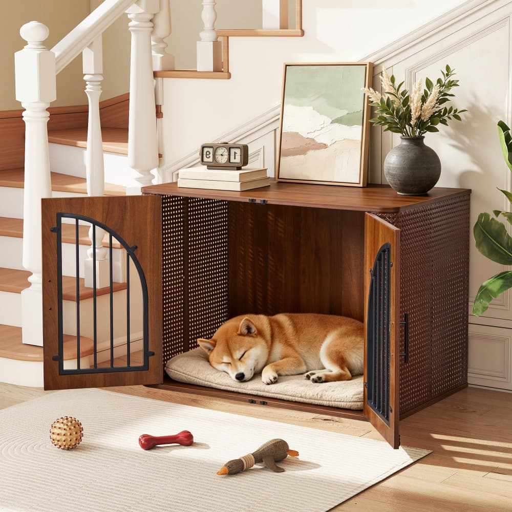 A brown wooden dog crate with open doors and a mesh front, shown in a staged home setting with a Shiba Inu sleeping inside on a cushion. The crate is placed on a rug on the floor of a staircase landing, with a vase, framed art, and a staircase visible in the background.