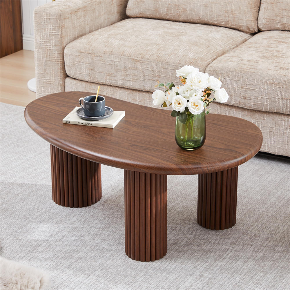Wooden coffee table with a vase of flowers and a cup on a light-colored rug in a living room.